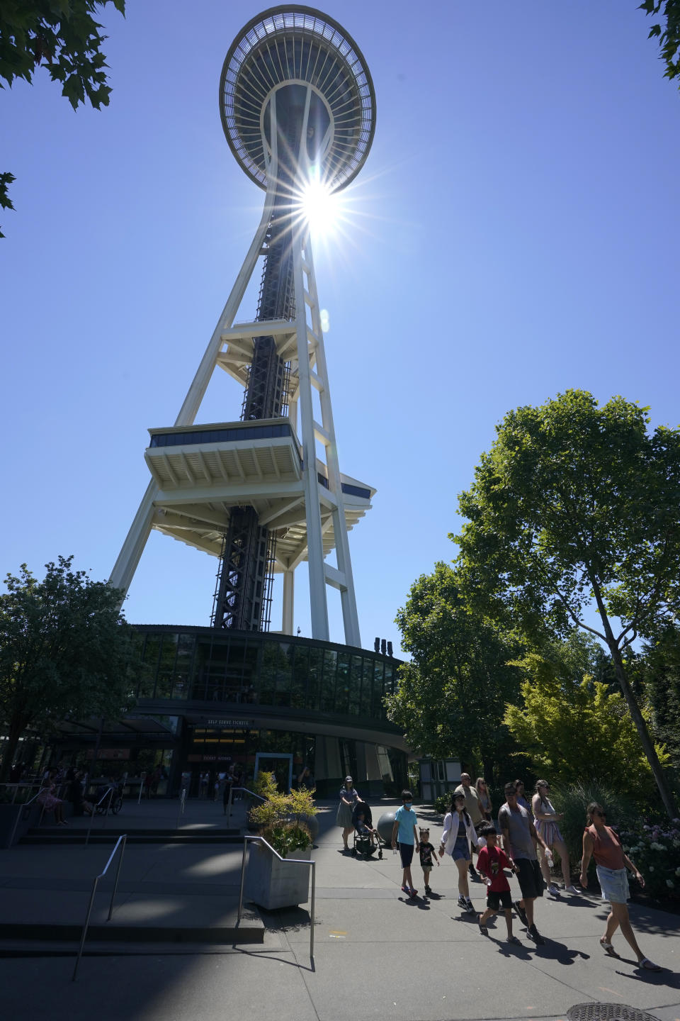 People walk as the sun shines behind the Space Needle, Monday, June 28, 2021, in Seattle. Seattle and other cities broke all-time heat records over the weekend, with temperatures soaring well above 100 degrees Fahrenheit (37.8 Celsius). (AP Photo/Ted S. Warren)