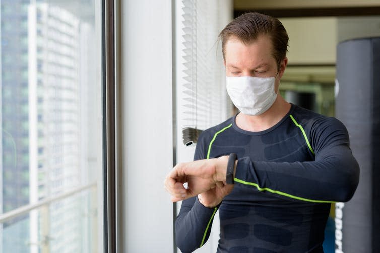 Man wearing a face mask checks his heart rate using his smart watch.