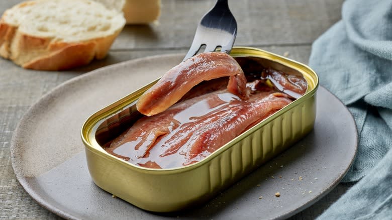 fork picking up piece of anchovy from can