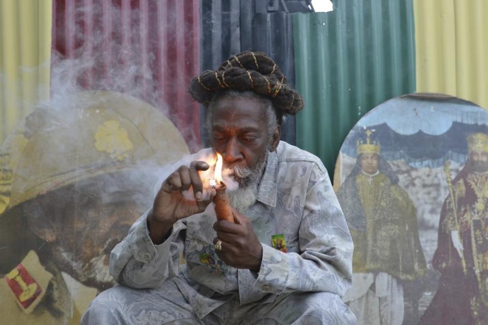 In this Aug. 28, 2014 file photo, legalization advocate and reggae legend Bunny Wailer smokes a pipe stuffed with marijuana during a “reasoning” session in a yard in Kingston, Jamaica. (AP Photo/David McFadden, File)