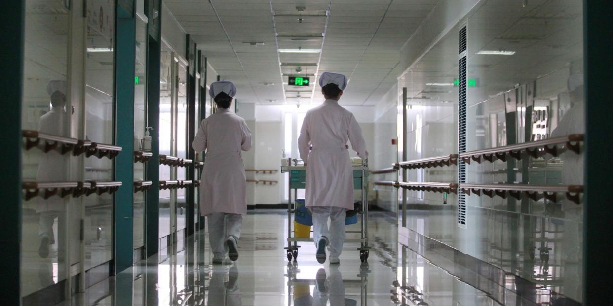 Nurses wheeling a medicine cart down a corridor.