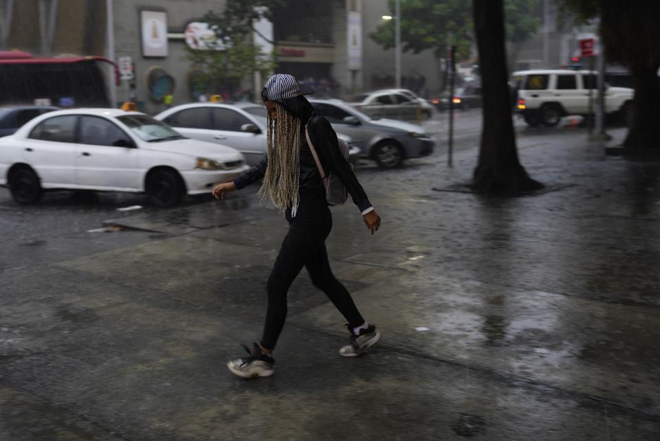 A woman walks under the rain in Caracas, Venezuela, Wednesday, June 29, 2022. As the latest tropical disturbance advances through the area, Venezuela shuttered schools, opened shelters and restricted air and water transportation on Wednesday as President Nicolas Maduro noted that the South American country already has been struggling with recent heavy rains. (AP Photo/Ariana Cubillos)