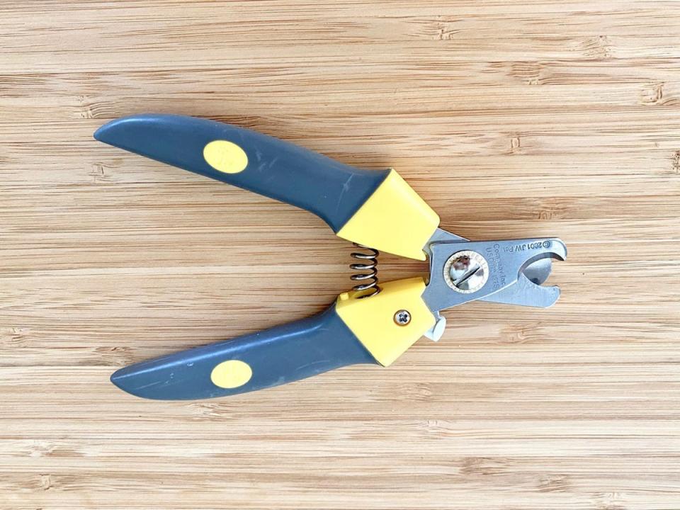 JW Pet nail clippers with black and yellow handles and steel blades sit on a wood surface.