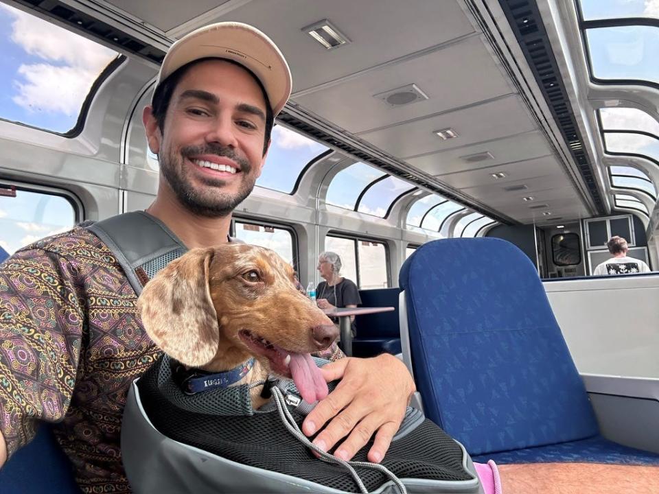 Sean and his dog Oliver, a brown dachshund, in the Amtrak observation car with large windows.
