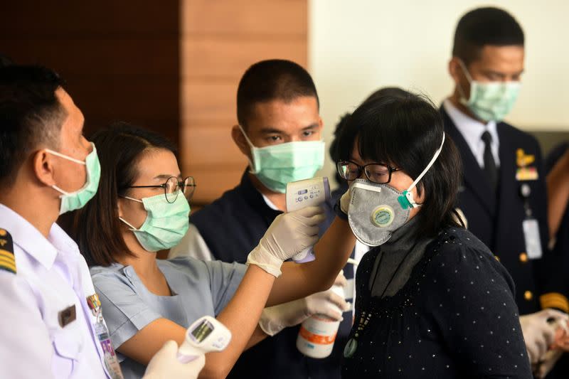 A health worker uses an infrared thermometer to check the temperature of a tourist who arrives at Bangkok's Don Mueang Airport