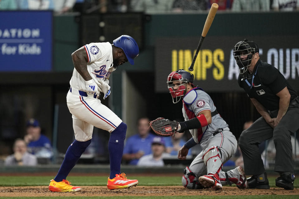Texas Rangers' Adolis Garcia, left, lets the bat loose after being hit by a pitch as Washington Nationals' Keibert Ruiz, center, and umpire Ryan Blakney look on in the fifth inning of a baseball game in Arlington, Texas, Tuesday, April 30, 2024. (AP Photo/Tony Gutierrez)