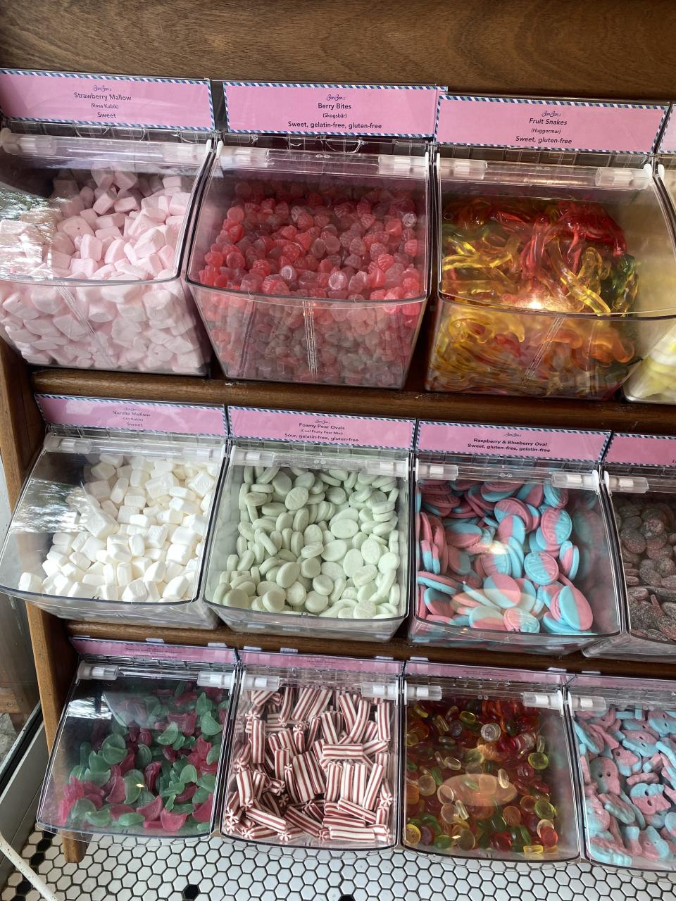 An assortment of candy displayed in clear bins, including gummy bears, peppermint sticks, and various shapes and sizes of gummies and hard candies