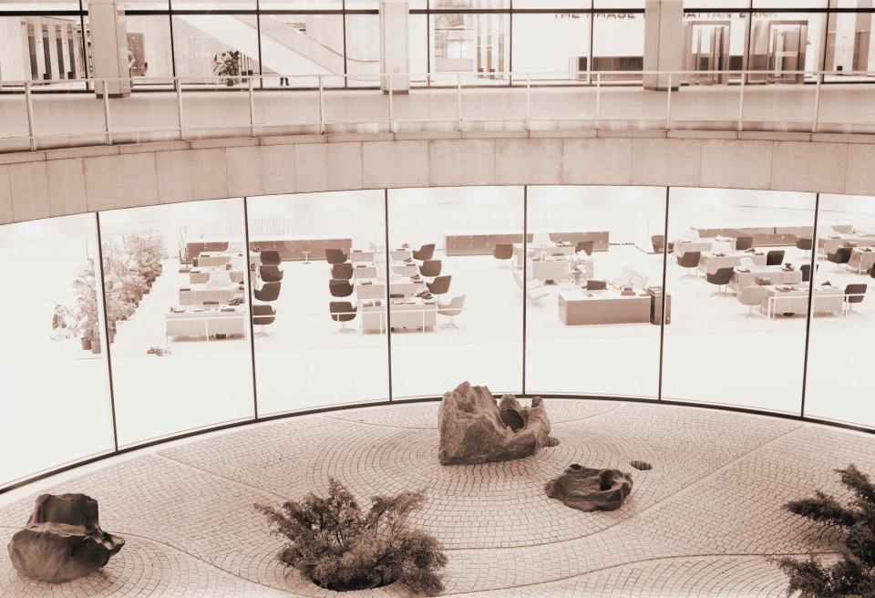 Rows of desks and chairs in an empty office surrounding an atrium rock garden, New York City.