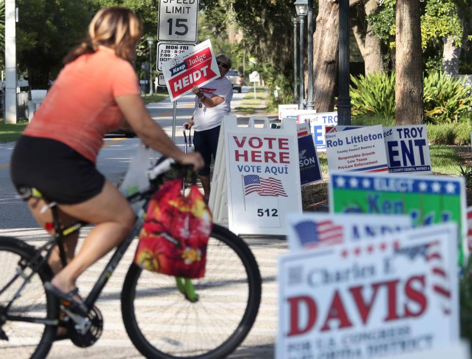 A bicyclist rides past dozens of campaign signs to enter the parking lot of the Ormond Beach Regional Library, where voters cast ballots in Tuesday's primary election. “We’ve got to stand up for democracy,” said voter Clenton Peterson, 65, an Army veteran and retired postal worker.