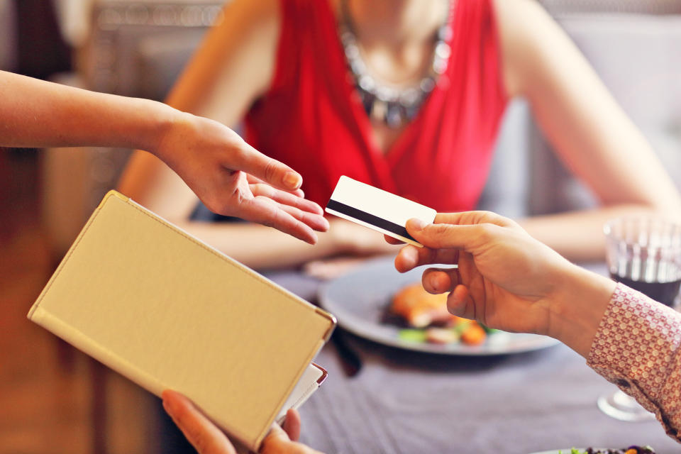 A person hands a credit card to a waiter to pay for their and their date's dinner