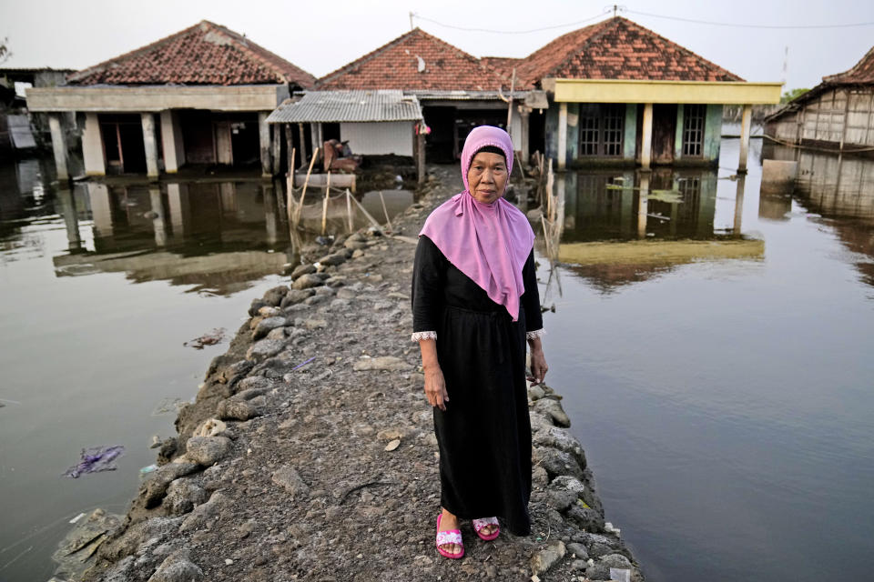 Kumaison stands on the pathway leading to her house in a flooded neighborhood in Timbulsloko, Central Java, Indonesia, Saturday, July 30, 2022. Kumaison says her home has been raised with concrete and dirt three times now, each time being followed by even higher flooding. (AP Photo/Dita Alangkara)