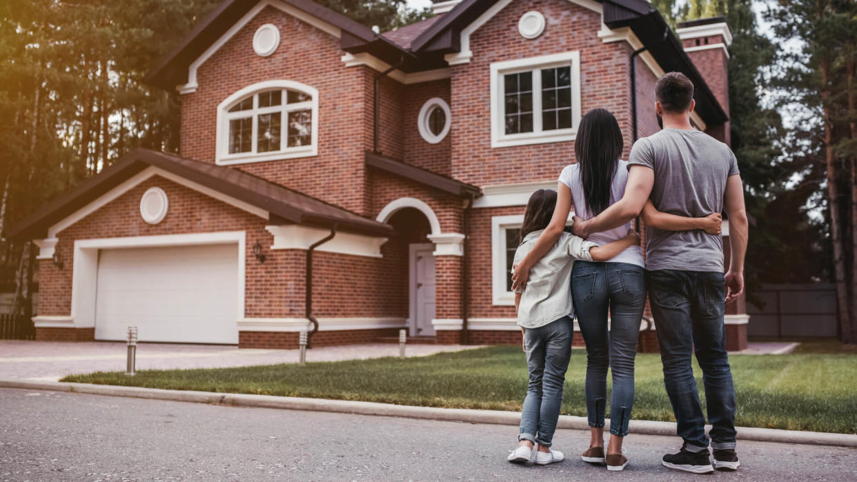 Back view of happy family is standing near their modern house and hugging.