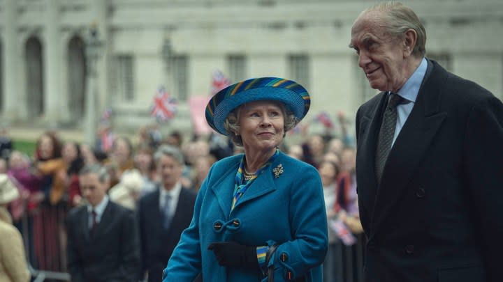 Queen Elizabeth II and Prince Phillip walking down the street, her smiling at him in a scene from The Crown season 6.