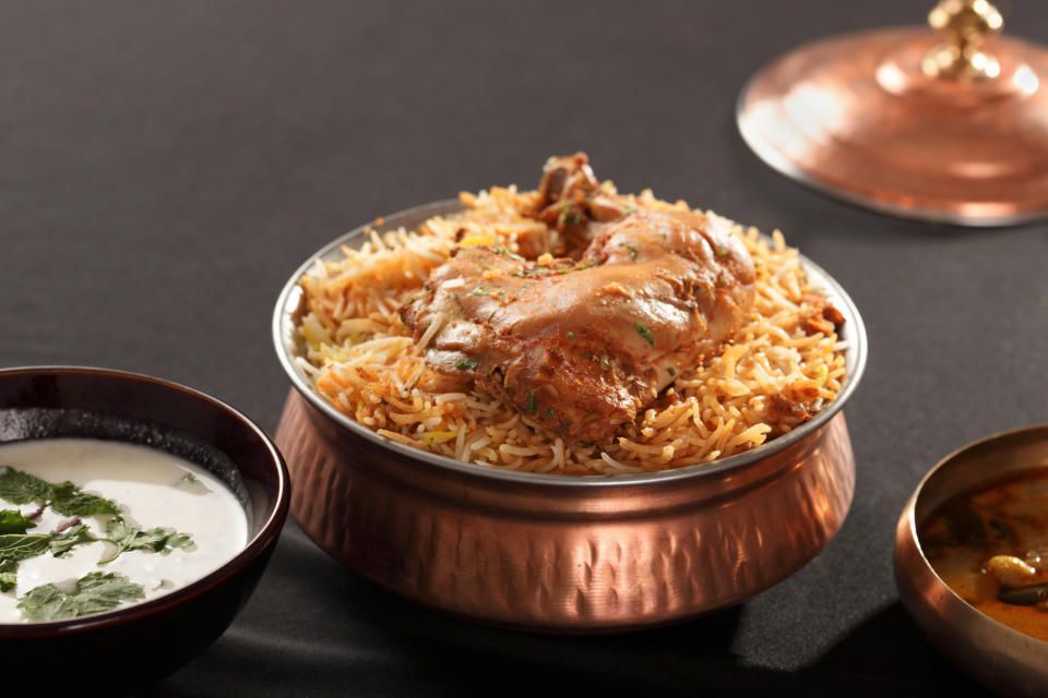 Chicken biryani, served in a copper bowl with a side of raita