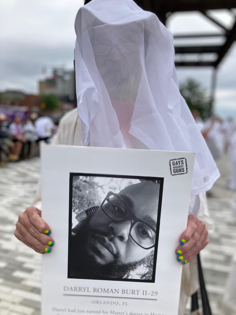 A protester dressed in white with a white veil holds a photo of Pulse shooting victim Darryl Roman Burt II with information about his life. 