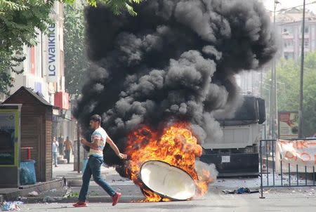 A man runs past a burning trash can, set on fire by protesters before a police vehicle, in the Kurdish dominated southeastern city of Diyarbakir, Turkey, September 13, 2015. REUTERS/Sertac Kayar