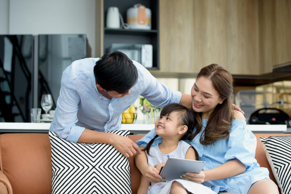 Asian family young parents sit on couch with daughter have fun using digital tablets together to watch funny videos in living room at home. Activities together and relationships in family concept.