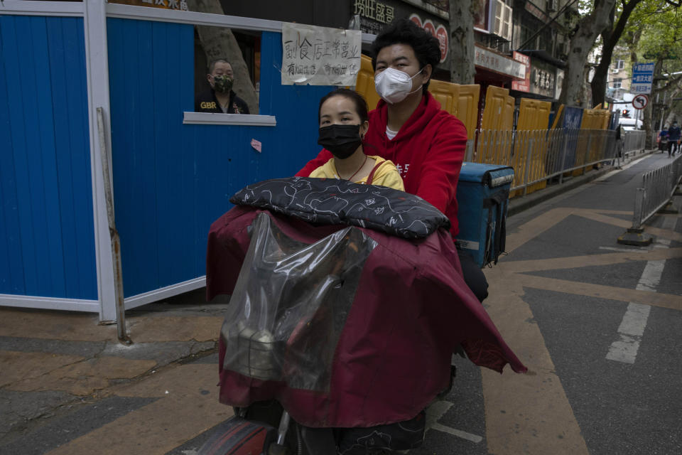 In this Wednesday, April 8, 2020, photo, residents wearing masks to help curb the spread the coronavirus pass by barricades around a community in Wuhan, central China's Hubei province. Released from their apartments after a 2 1/2-month quarantine, residents of the city where the coronavirus pandemic began are cautiously returning to shopping and strolling in the street but say they still go out little and keep children home while they wait for schools to reopen. (AP Photo/Ng Han Guan)