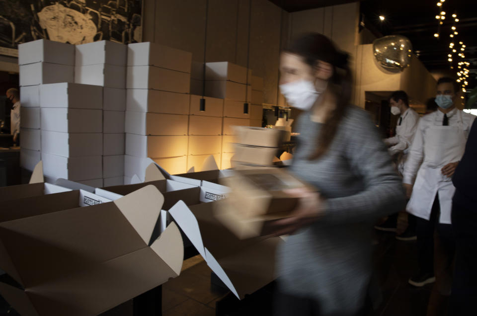 A staff member carries dinner boxes as she prepares part of nearly 600 take-away orders at Sergio Herman's Le Pristine restaurant in Antwerp, Belgium, Saturday, Nov. 7, 2020. Of all the many challenges the pandemic throws up for all kinds of professions, this one has been particularly tough: How to put a three-star chef into a takeout box. (AP Photo/Virginia Mayo)