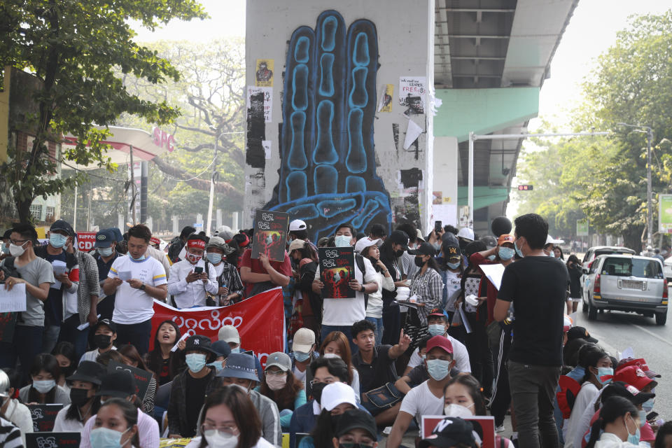 Protesters gather in front of three-fingered salute graffiti during an anti-coup protest in Sanchaung township, outskirt of Yangon, Myanmar, Sunday, Feb. 21, 2021. Police in Myanmar shot dead a few anti-coup protesters and injured several others on Saturday, as security forces increased pressure on popular revolt against the military takeover. (AP Photo)