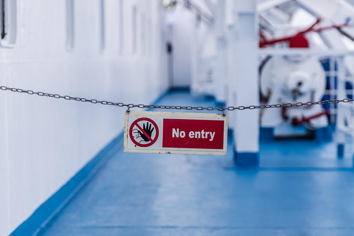 No entry warning sign in red colour. It is attached with a chain on the outside of a ship.