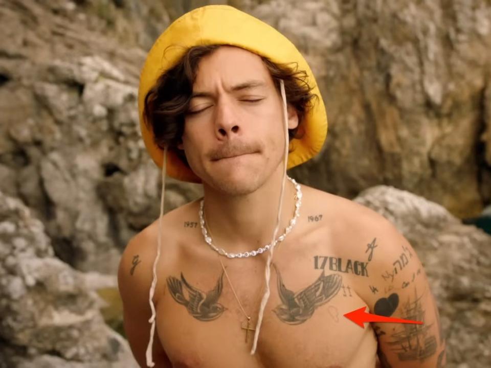 A red arrow pointing to a tattoo of a half of a broken heart, seen in Harry Styles' music video for "Golden."