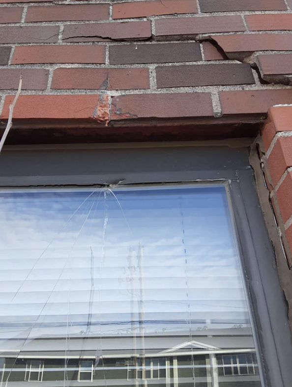 A broken window in a brick wall, showing signs of damage in the upper left corner.