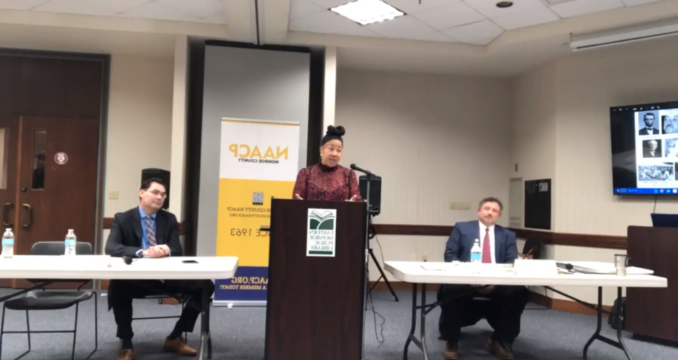 Christa Caceres, president of the Monroe County chapter of the NAACP, speaks at the beginning of a forum between district attorney candidates Donald Leeth, left, and Michael Mancuso, right.