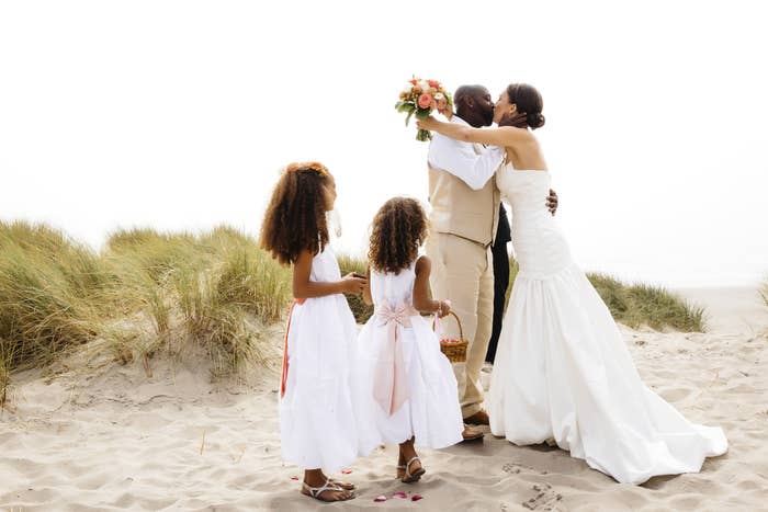 A couple getting married kisses on the beach while two flower girls look on