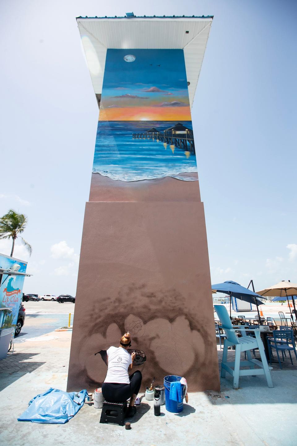 Summer DeSalvo paints the bottom of a mural on Fort Myers Beach on Monday, July 24, 2023. The mural is on a three-story elevator shaft left standing after Hurricane Ian in Times Square.