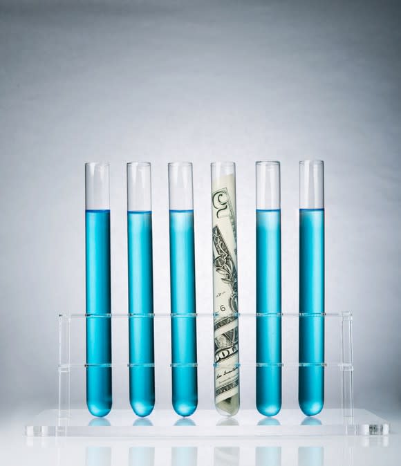 Six test tubes, five with a blue liquid and one stuffed with cash