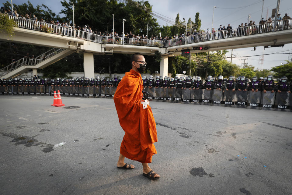 A monk walk pass police blocking protesters in a main intersection as he returns to his temple near the Parliament in Bangkok, Tuesday, Nov. 17, 2020. Thailand's political battleground shifted to the country's Parliament Tuesday, where lawmakers are considering proposals to amend the country's constitution, one of the core demands of the student-led pro-democracy movement. (AP Photo/Sakchai Lalit)
