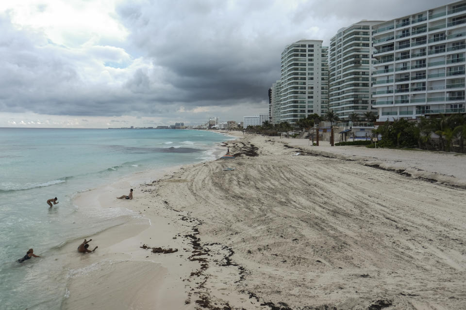 The beach is empty where a few tourists spend time on the waters' edge in Cancun, Mexico, Saturday, June 13, 2020. An irony of the coronavirus pandemic is that the idyllic beach vacation in Mexico in the brochures really does exist now: the white sand beaches are sparkling clean and empty on the Caribbean coast. (AP Photo/Victor Ruiz)