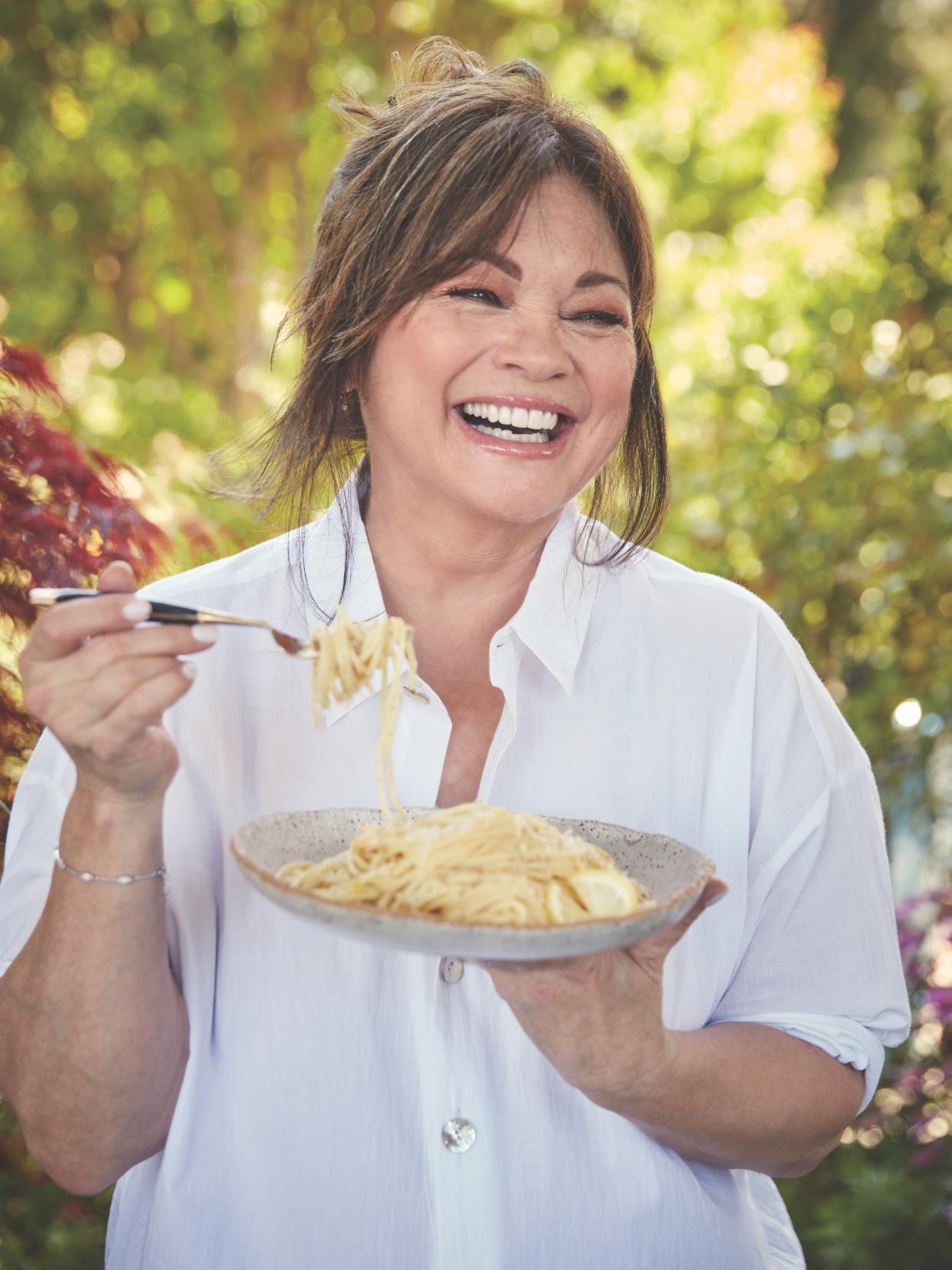 Valerie Bertinelli  holding a plate of pasta with one hand and a forkful of it in the other.