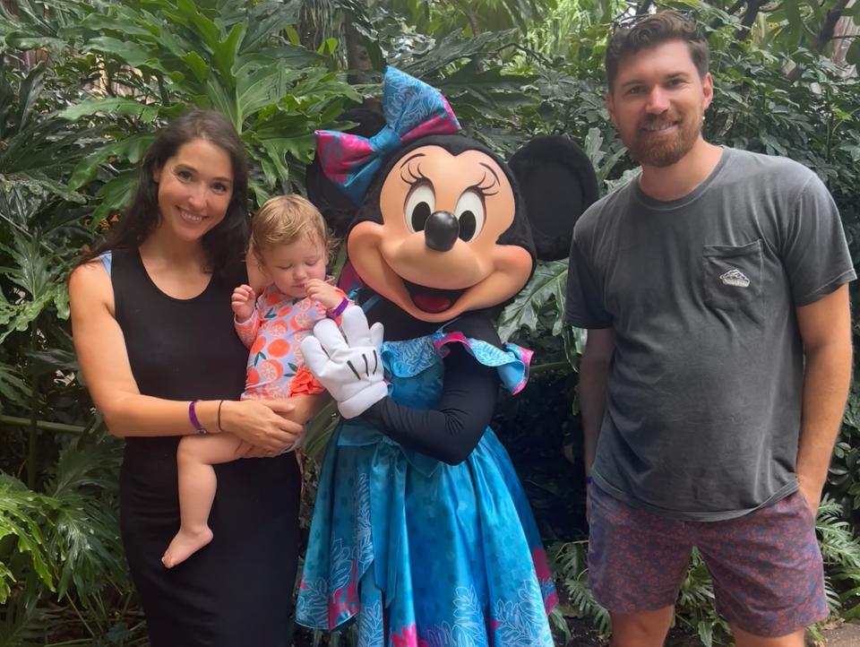 A man, woman, and baby take a picture with minnie mouse