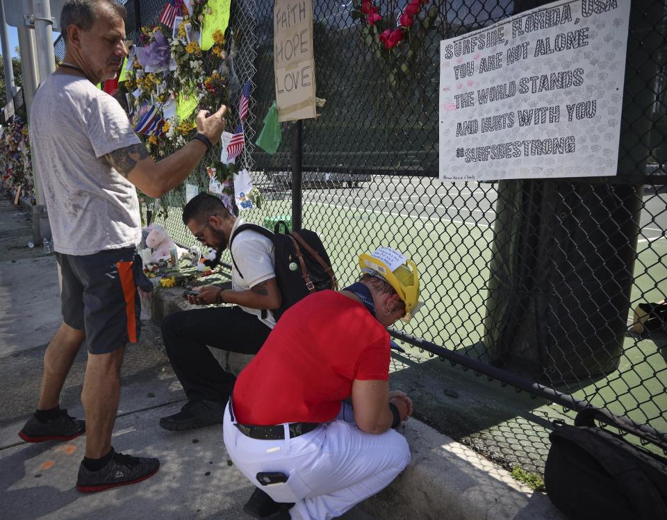 Hialeah resident Alison Kairuz, right, bows her head in prayer after pinning her hand-made sign to the fence in support of families and friends who lost love ones at the memorial site for victims of the partially collapsed South Florida condo building Champlain Towers South, in Surfside, Fla., Sunday, July 4, 2021. (Carl Juste/Miami Herald via AP)