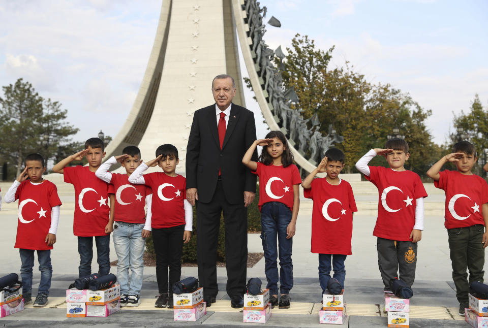 Turkish President Recep Tayyip Erdogan poses for photos with primary school students from a village of Black Sea city of Samsun, who give a military style salute outside the presidential palace, in Ankara Monday, Oct. 21, 2019. Erdogan has responded angrily to widespread criticism in the West of Turkey's incursion in northeast Syria.(Presidential Press Service via AP, Pool )