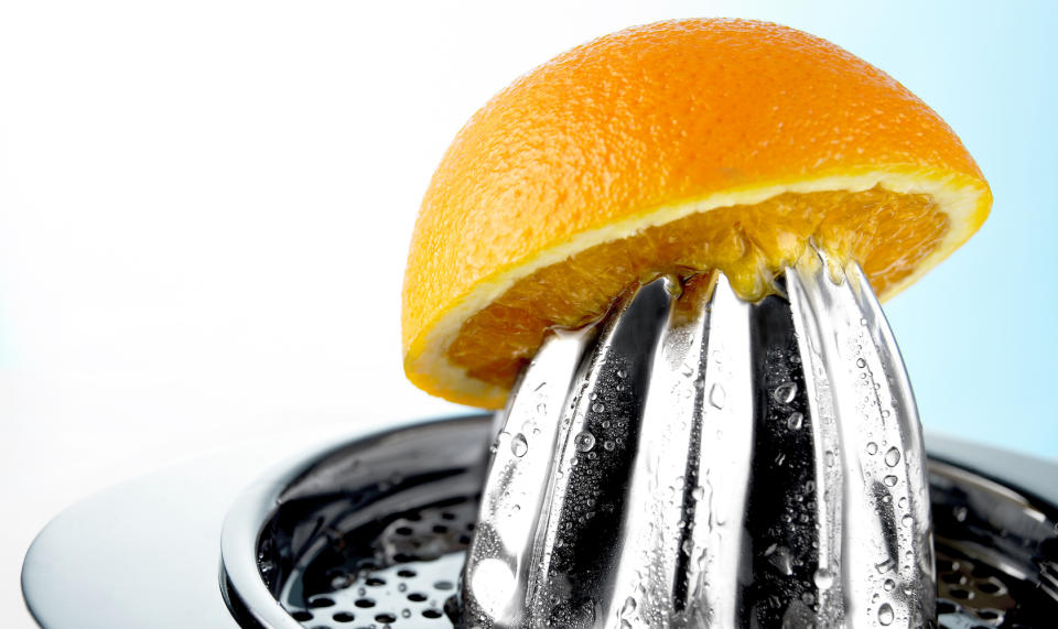 half of an orange balanced atop a metal juicer