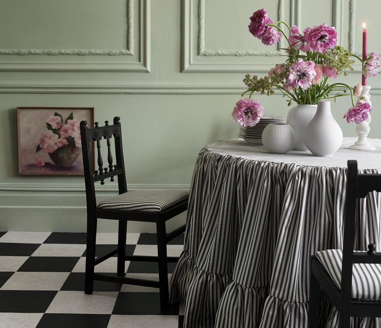  A dining room with a checkerboard flooring and ticking stripe upholstered chairs and tablecloth. 