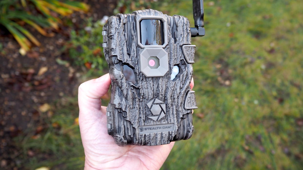  Stealth Cam Fusion Global Trail Camera held in a hand over grass. 