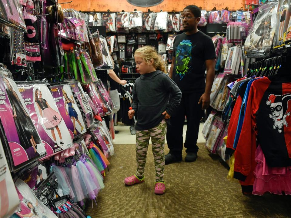 A young girl shops for Halloween costumes with her father at Spirit Halloween.