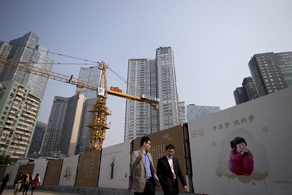 FILE - In this Oct. 8, 2013 file photo, office workers walk past China Dream propaganda boards, showing messages pushed by the current Chinese President Xi Jinping's administration, on display near a construction site in Beijing, China. Economists fear a lending bubble in China could threaten the global economy unless the Chinese government shores up its financial system, according to an Associated Press survey. (AP Photo/Andy Wong, File)