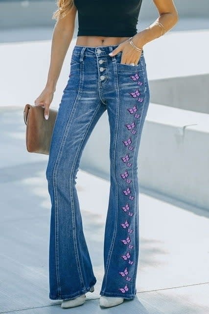 Person in denim bell-bottoms with floral embroidery, paired with a black top, holding a brown clutch