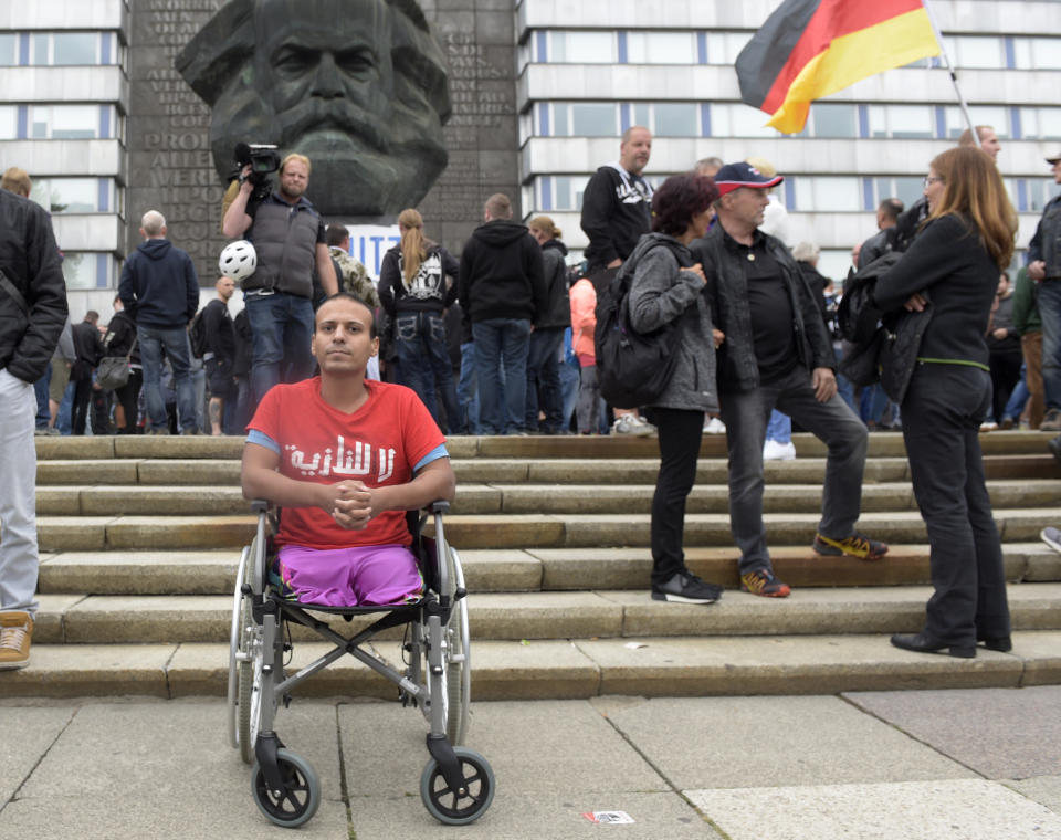 A man wears a t-shirt with the Arabic writing 'No Nazis' as he sits in a wheelchair in front of the Karl Marx statue in Chemnitz, eastern Germany, Saturday, Sept. 1, 2018, after several nationalist groups called for marches protesting the killing of a German man last week, allegedly by migrants from Syria and Iraq. (AP Photo/Jens Meyer)