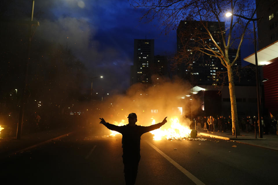 A protester walks past burning garbages during a protest in Paris, Saturday, March 18, 2023. A spattering of protests were planned to continue in France over the weekend against President Macron's controversial pension reform, as garbage continued to reek in the streets of Paris and beyond owing to continuing action by refuse collectors. (AP Photo/Lewis Joly)