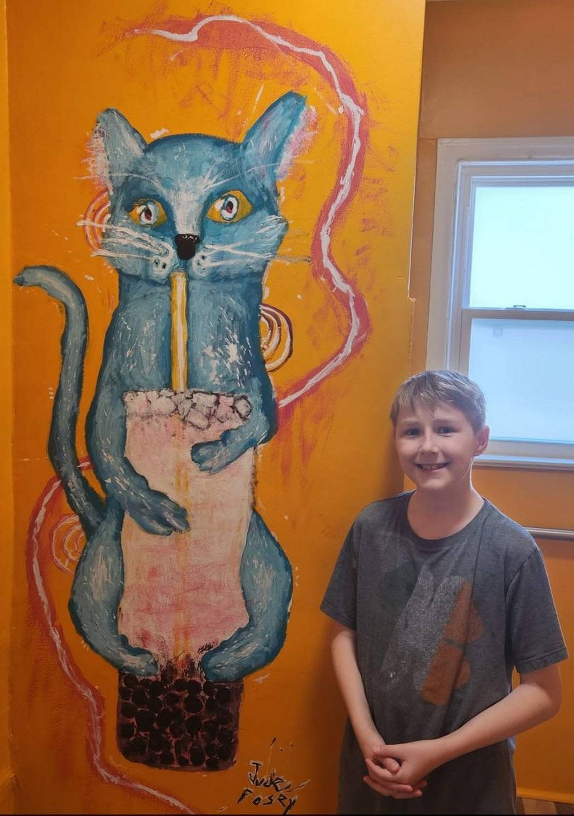 Noah Posey stands next to his artwork inside the Right Meow Cat Cafe restroom. He and his brothers assist Kayleigh and Damion with the operations of the new cafe.