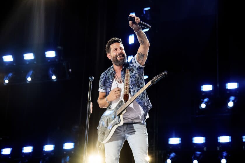 Matthew Ramsey of Old Dominion raises his left hand onstage while performing with a guitar