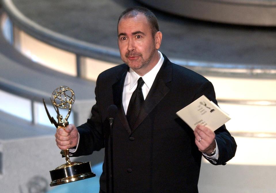 Terence Winter holds an Emmy in one hand and a winner's envelope in the other onstage.