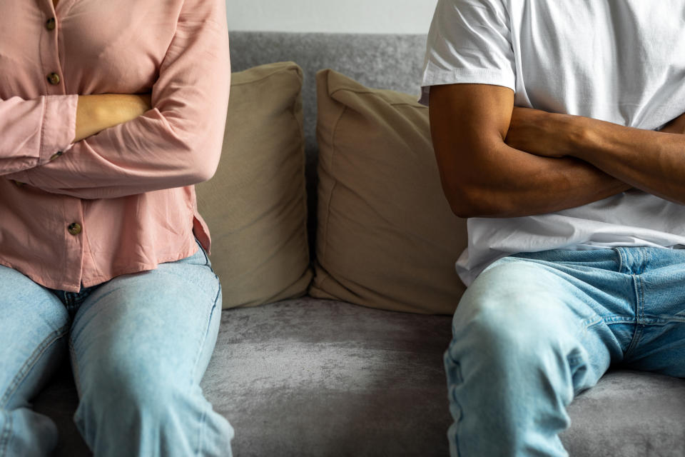 Two people sitting on a couch with arms crossed, facing away from each other, suggesting disagreement or conflict