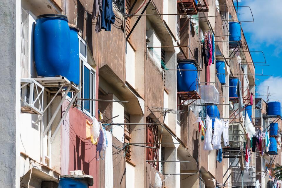 An apartment building with large blue water barrels sitting outside each unit on platforms similar to where you'd see a window air conditioner.